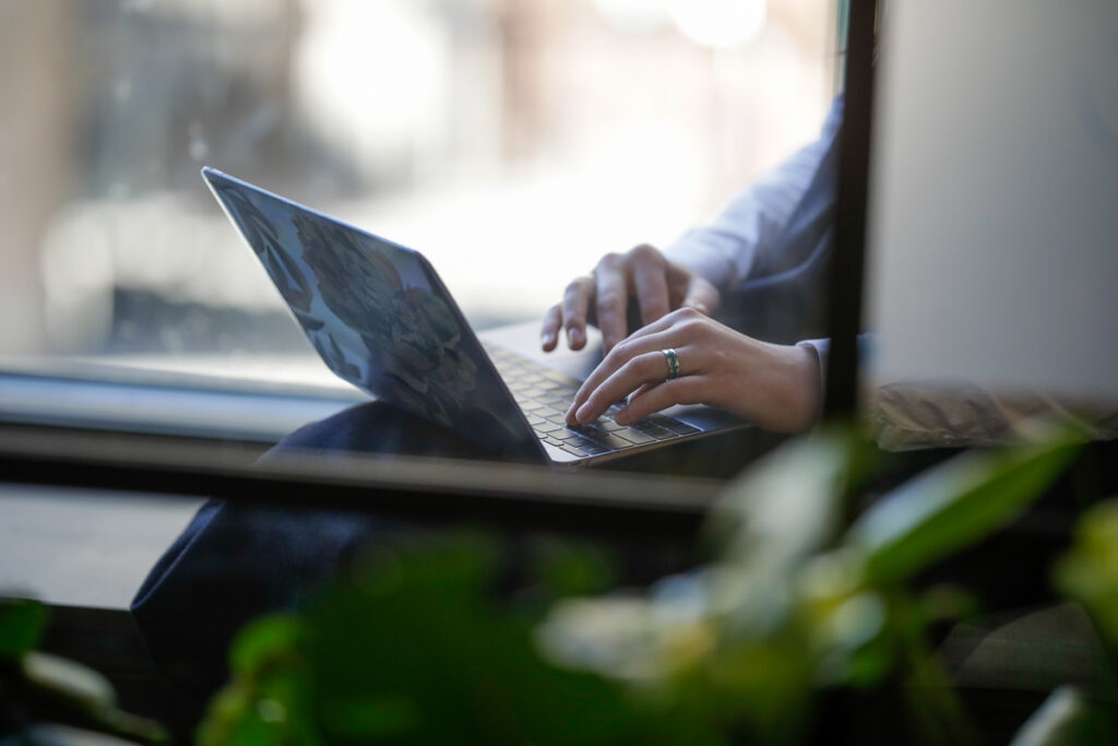 Foto av hender på en mac og med planter som stikker opp foran